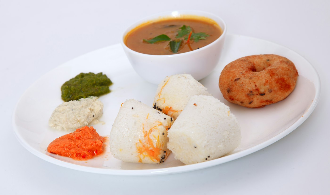 Idli, medu vada and sambar on a white plate