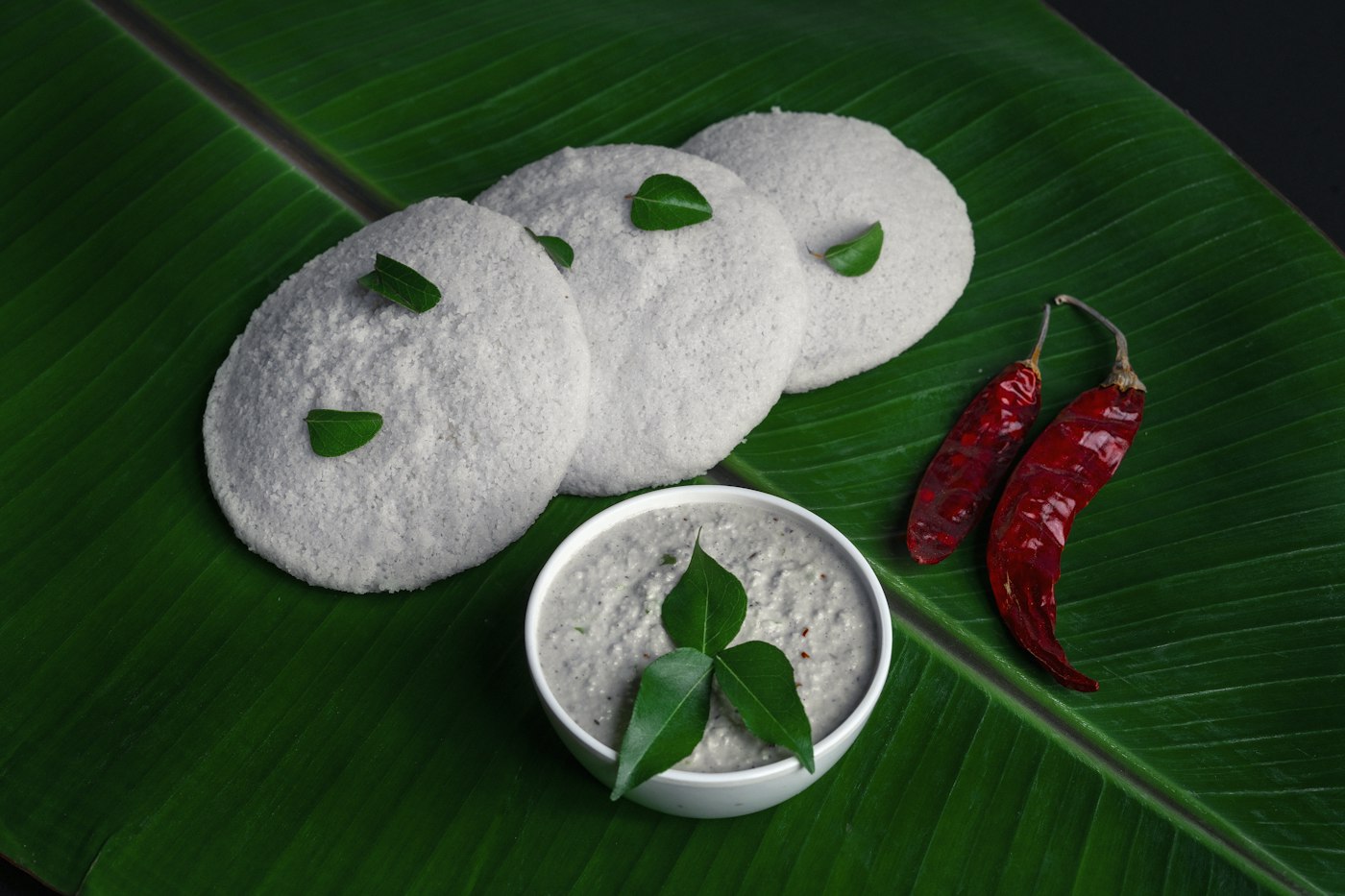 Soft steamed idlis with coconut chutney, served on a banana leaf